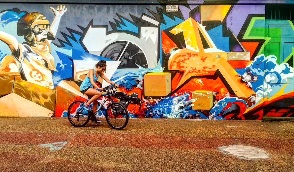 昼間、落書きの壁の横で自転車に乗る女性