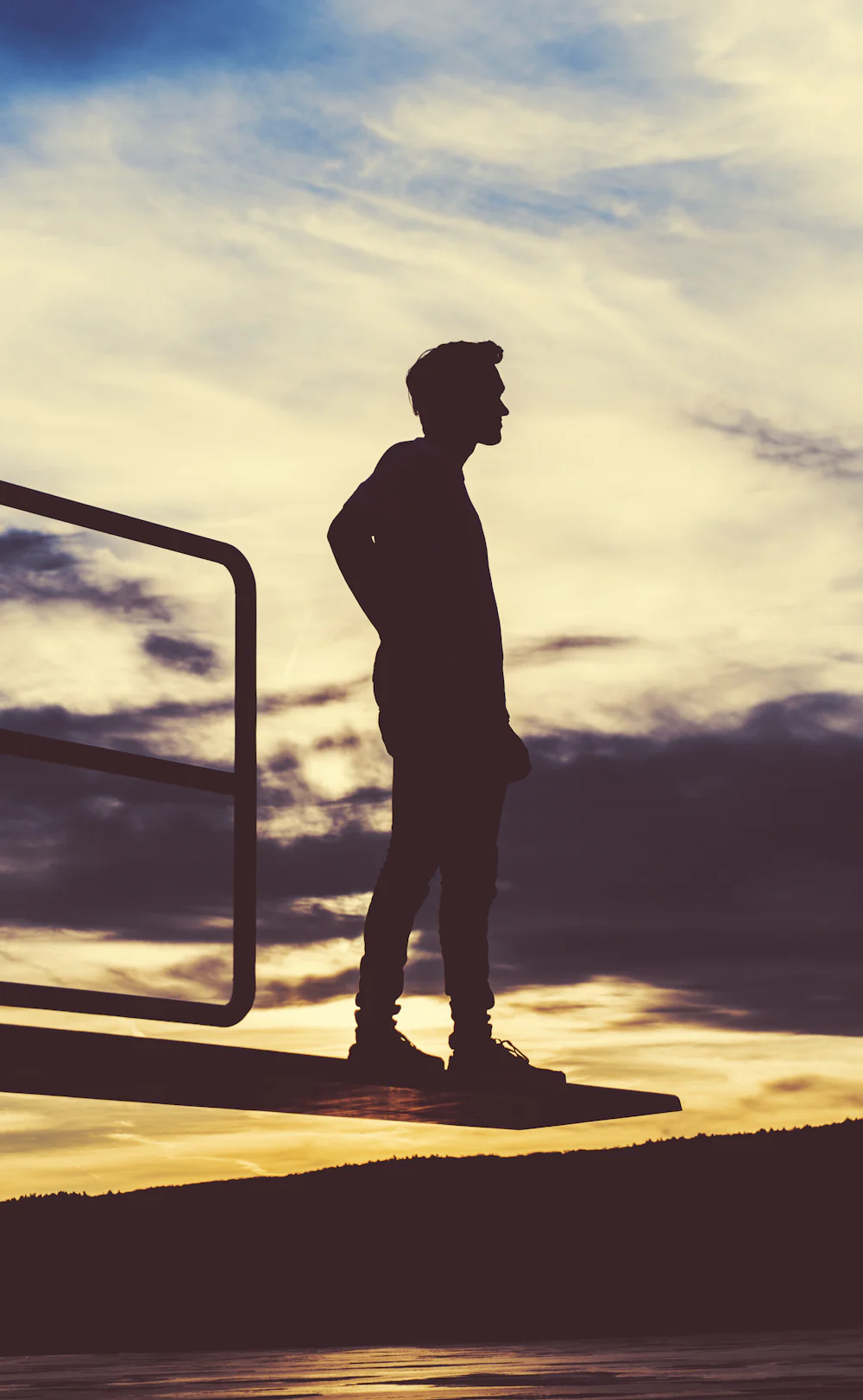 A lone figure standing at the edge of the water at dusk, facing away from the camera.
