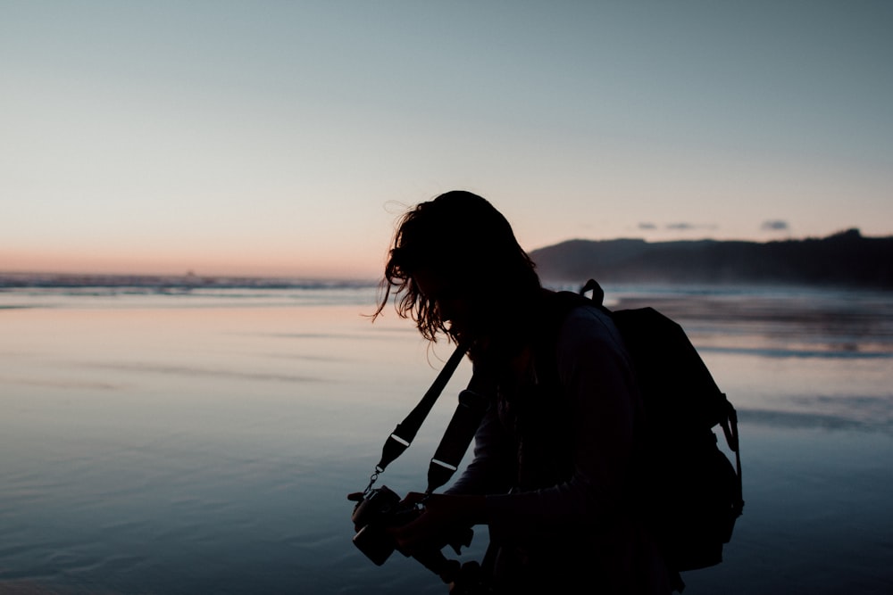silhouette photo of man holding a camera beside body of water