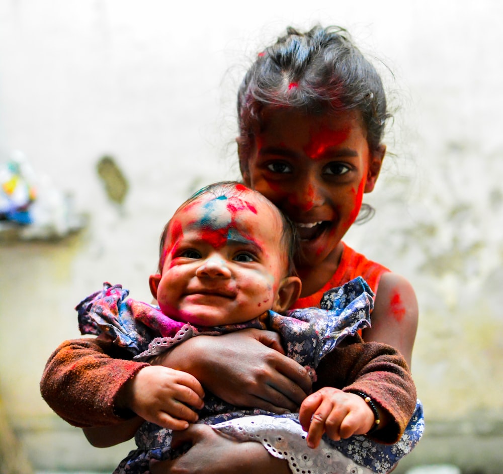 girl wearing red tank top carrying baby