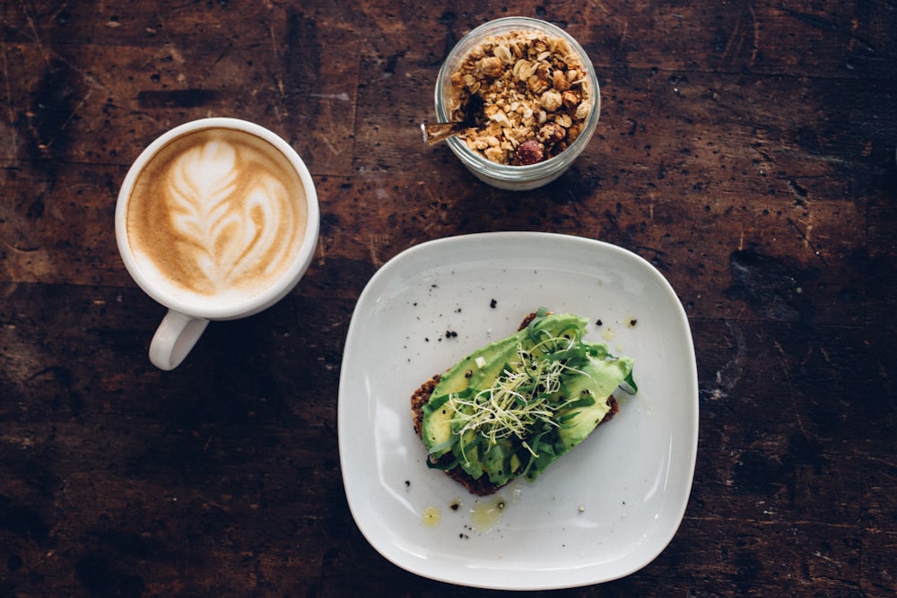 sliced vegetable on plate near coffee cup and nuts on glass container