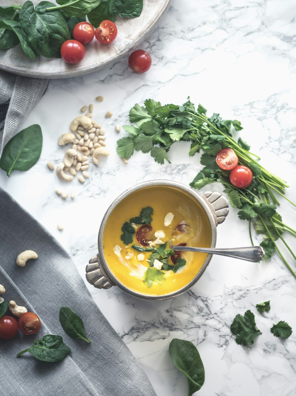 Sopa de crema amarilla cubierta con verduras de hoja verde en un cuenco redondo de cerámica gris