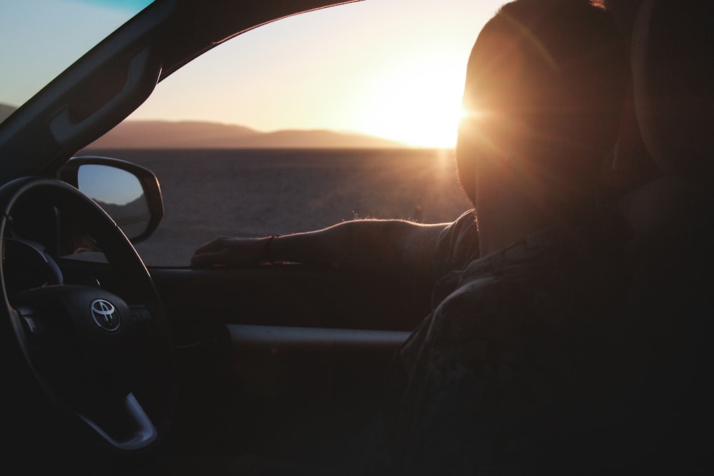 夕日を眺めながらトヨタ車に乗る男性のシルエット