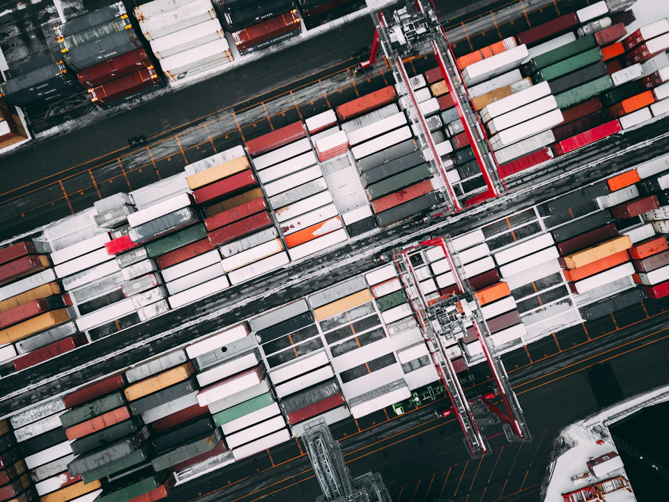 Bustling shipping yard with numerous stacked containers and two large cranes in foreground operation