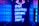 A neon sign with vibrant blue illumination displays the words 'BAR,' 'COCKTAILS,' 'DREAMS,' 'DISCO,' and 'PARTY.' Above the sign, a purple neon arrow points downward. The setting appears to be a dimly lit corridor or entrance to a venue, with walls reflecting the blue glow.
