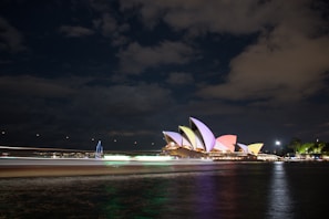 Sydney Opera House illuminated at night with reflections shimmering on the harbor water.