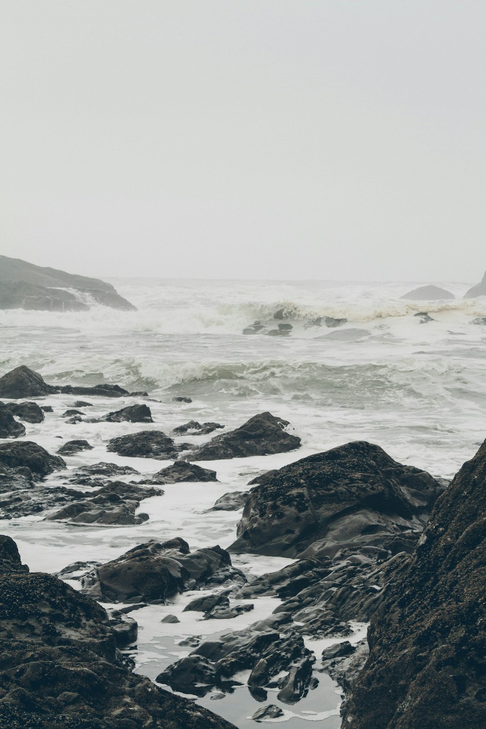 black rock formation near body of water under white sky