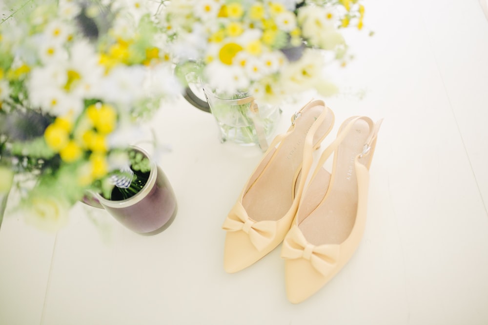 Par de zapatos de tacón destalonados beige de punta puntiaguda para mujer con cintas cerca del jarrón de flores
