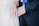 Two hands are shown overlapping. Both wear rings, suggesting a wedding or commitment ceremony. One person is dressed in a dark suit with a blue tie, while the other wears a light-colored outfit.