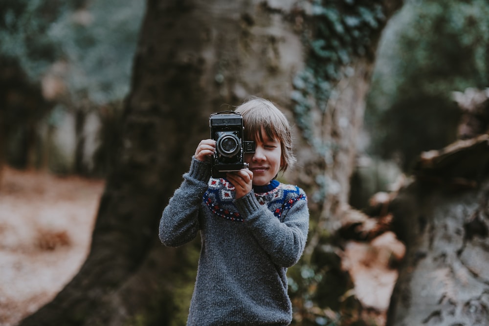 Junge mit Kamera in der Nähe eines braunen Baumes während des Tages