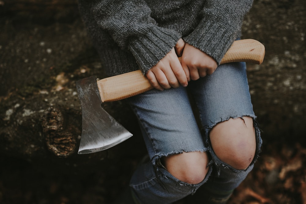 person wears grey knit sweatshirt sitting down while holding brown axe