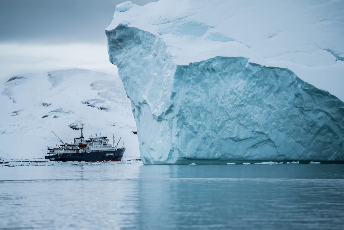 An expedition vessel in Arctic waters beside ice and dark cliffs