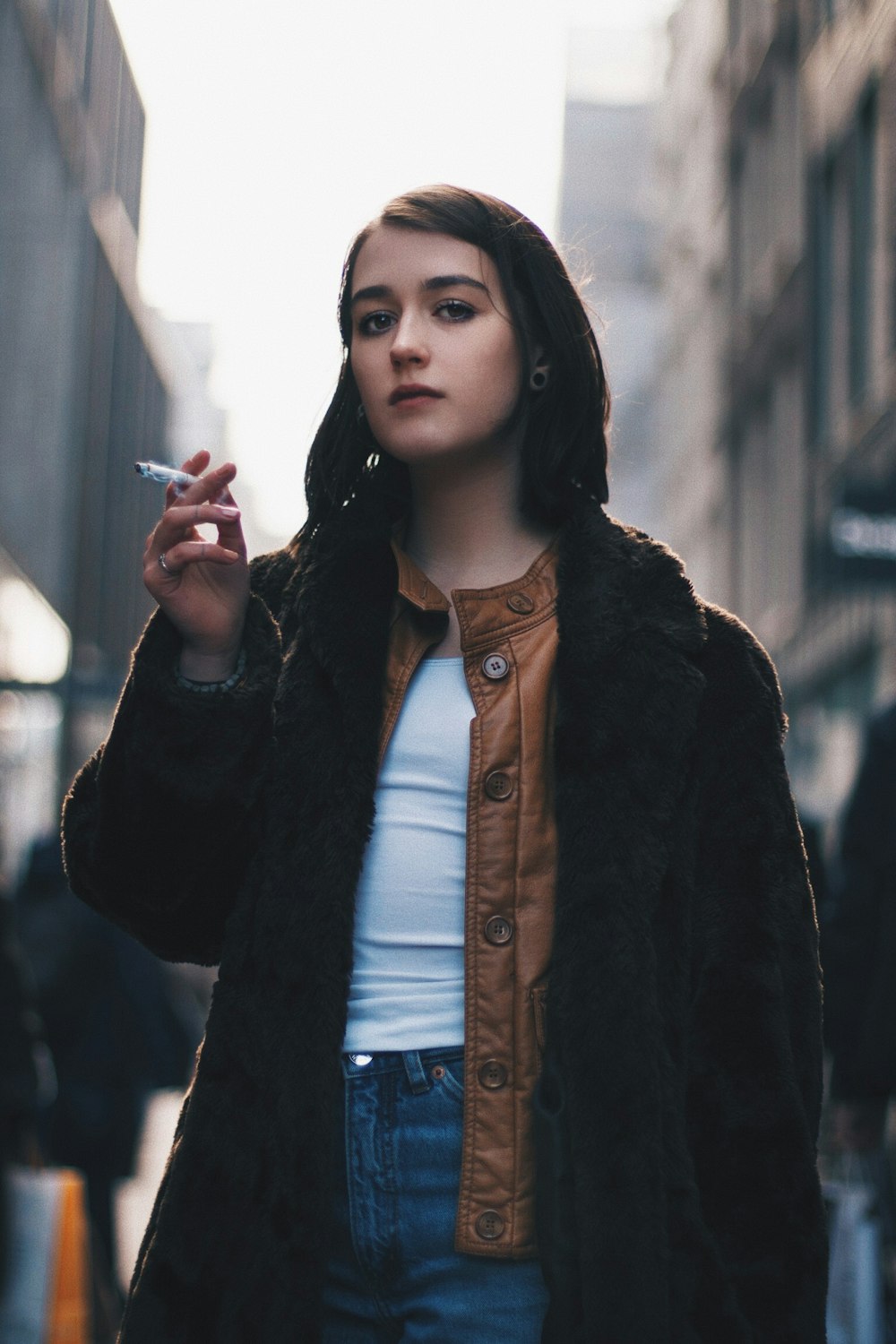 mulher vestindo casaco preto e segurando o bastão de cigarro durante o dia