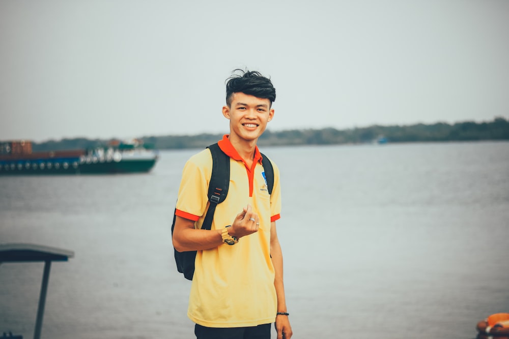 person standing near body of water while doing finger heart hand gesture at daytime