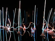 An outdoor artistic installation illuminated with green and aqua lights against a night sky.