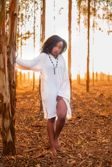 A serene pregnant woman walking barefoot along a quiet forest path at dawn, sunlight filtering through the trees.