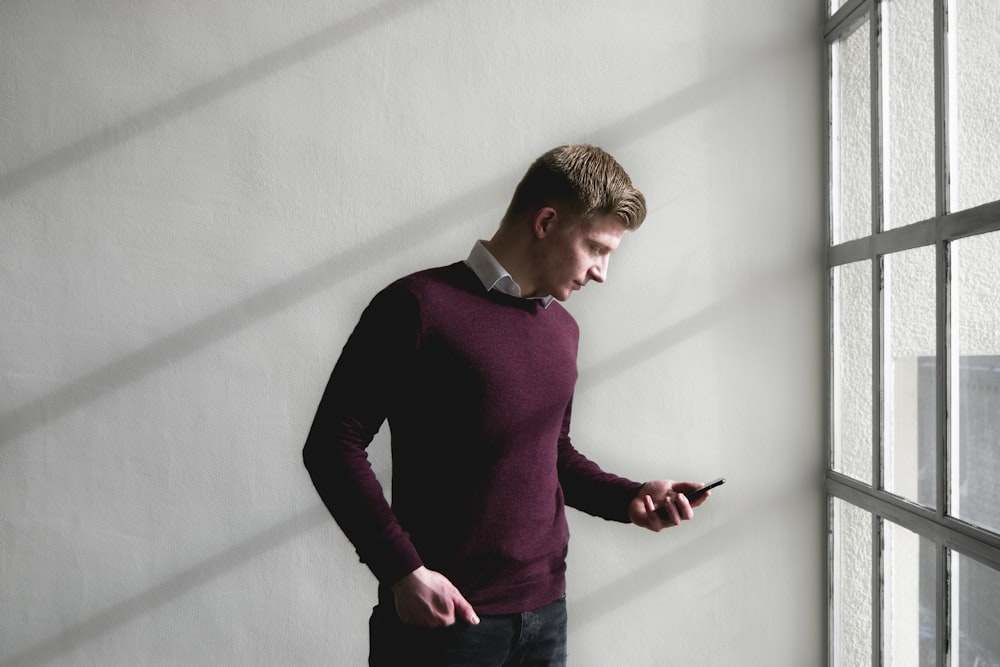 man standing near white concrete wall while using smartphone