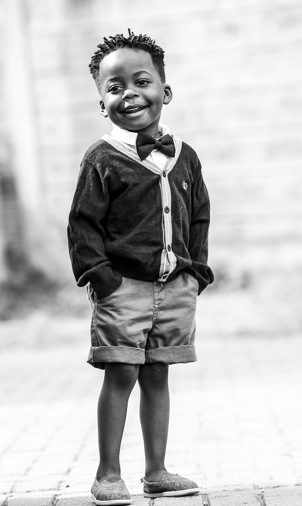 Foto en escala de grises de un niño con cárdigan negro abotonado y pantalones cortos