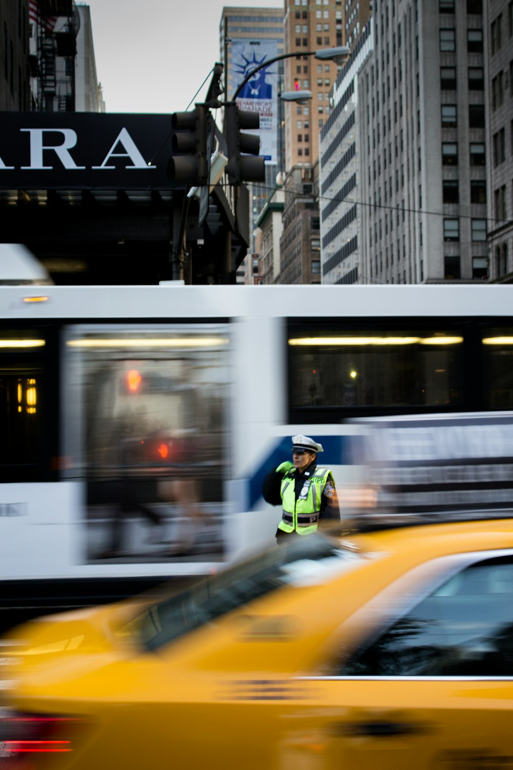 photo of man in green safety vest and white peak cap standing in between white bus and orange car