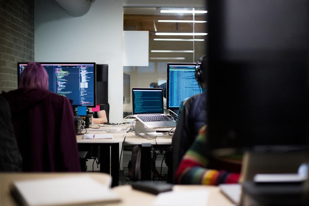 Two employees sitting next to each other in an office space with their monitors placed in front of them.