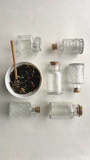 A collection of glass jars with cork stoppers arranged on white sand, capturing the light of a sunny Ibiza afternoon.