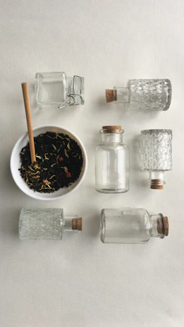 A collection of glass jars with cork stoppers arranged on white sand, capturing the light of a sunny Ibiza afternoon.