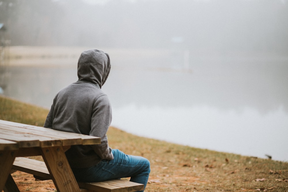 person in gray hoodie sitting on picnic table staring at the fog during daytime