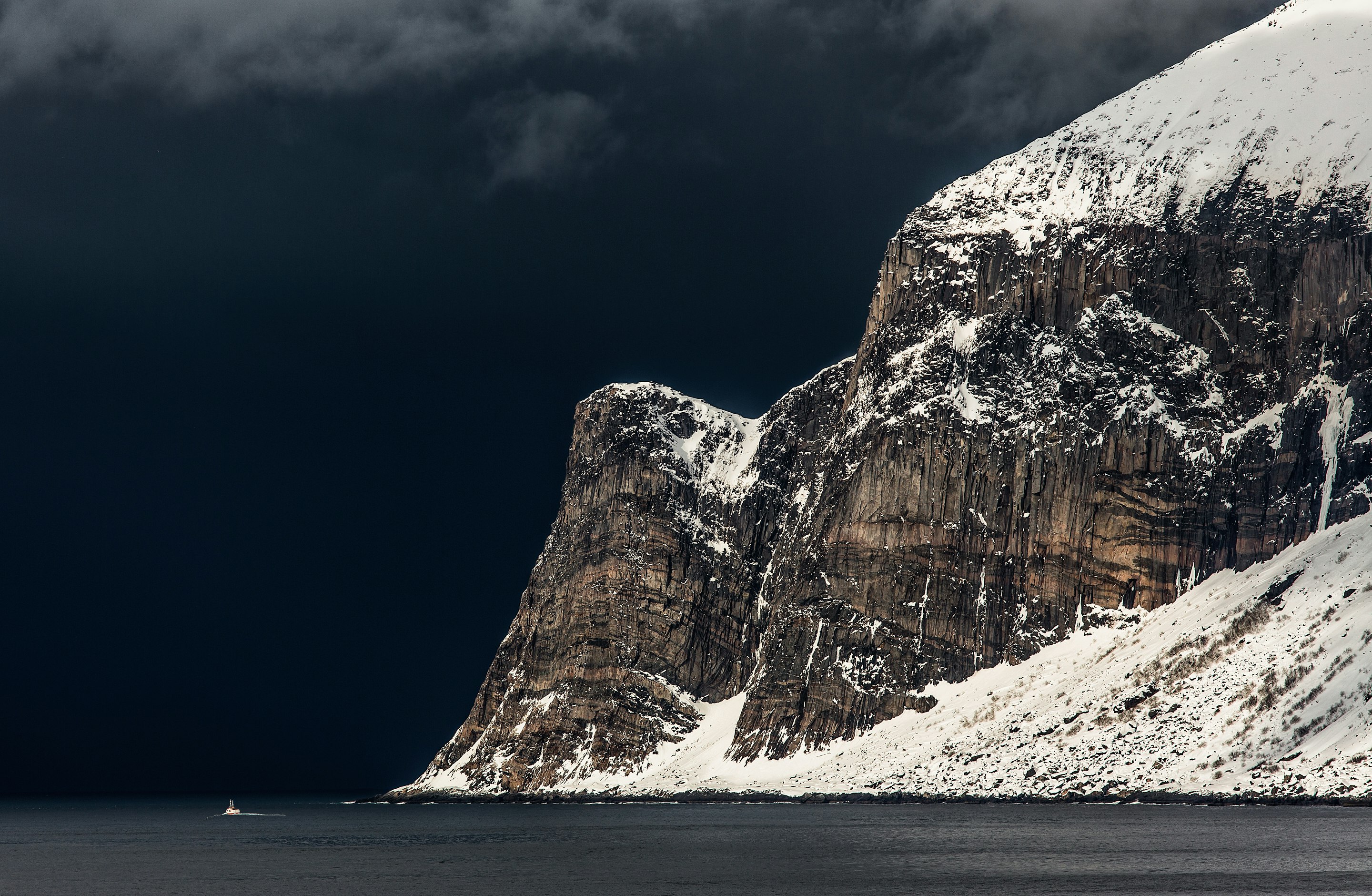 black mountain covered by snow near body of water