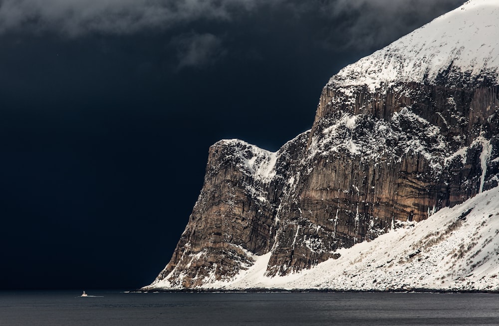 black mountain covered by snow near body of water