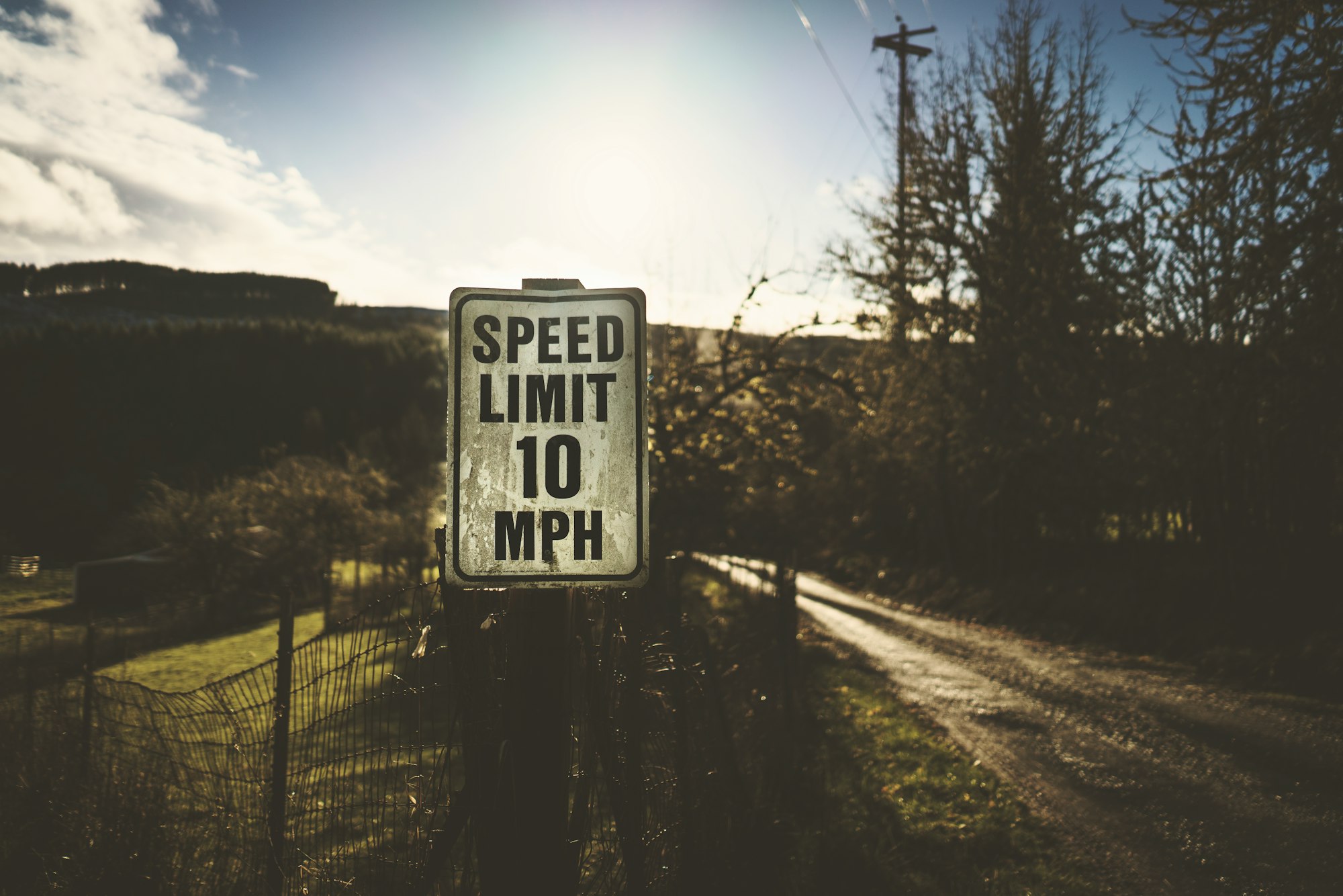 a sign reading "speed limit 10 mph" by a fence at the side of a rural road