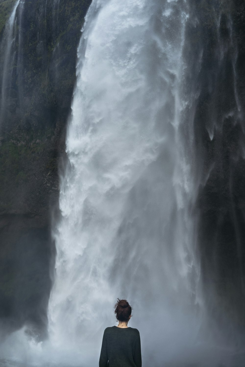 滝のそばに立つ黒い長袖シャツを着た女性
