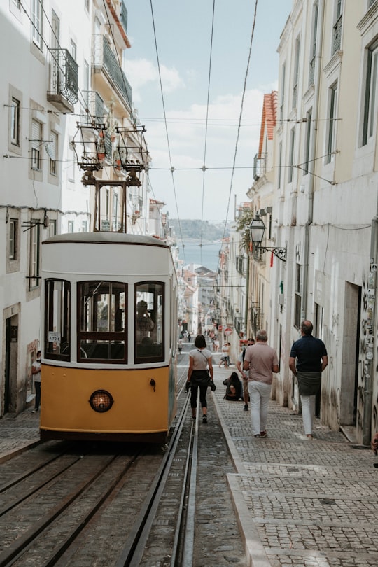 thee person walking near white and orange bus in Elevador da Bica Portugal