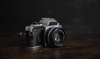 A close-up shot of a vintage camera resting on a matte black surface with soft cream highlights.