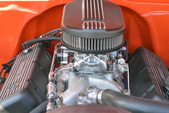 An engine with a prominent air filter on top, surrounded by various metallic components and fittings. The engine is set within a bright orange backdrop, highlighting its complex mechanical structure.