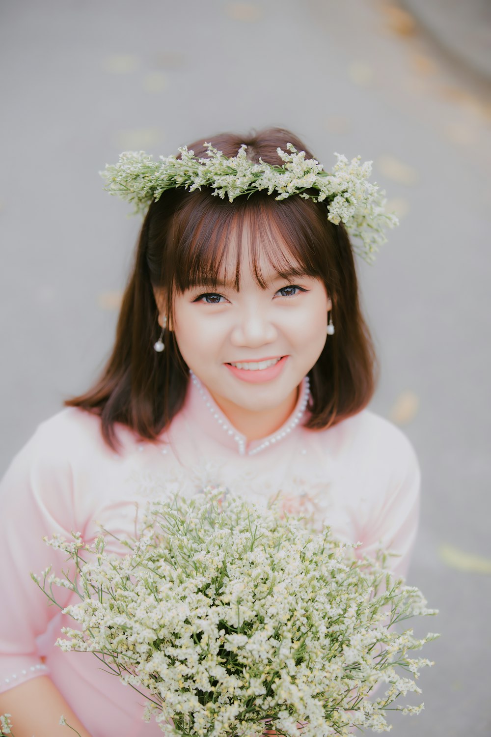 woman wearing pink top with white petaled flower headrest and holding white flower bouquet