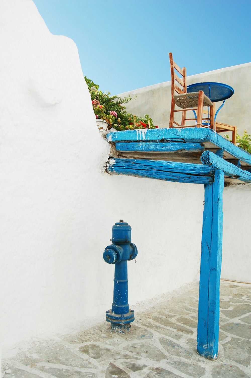 blue hydrant under blue wooden loft with chair on top under blue sky at daytime