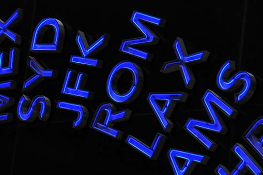 A collection of bold, three-dimensional uppercase letters with a glowing blue outline on a dark background. The letters appear to represent airport codes, including JFK, LAX, and AMS, arranged in a dynamic and slightly overlapping manner.
