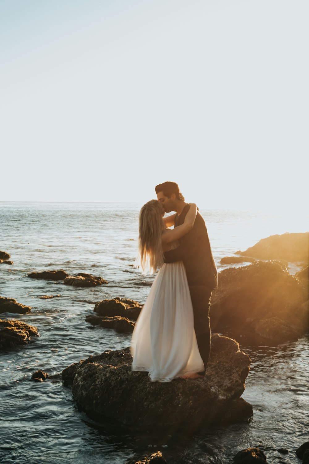 man and woman kissing on top of gray rock at beach