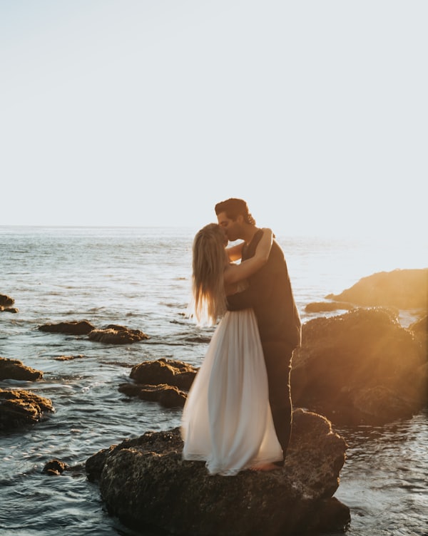 man and woman kissing on top of gray rock at beach