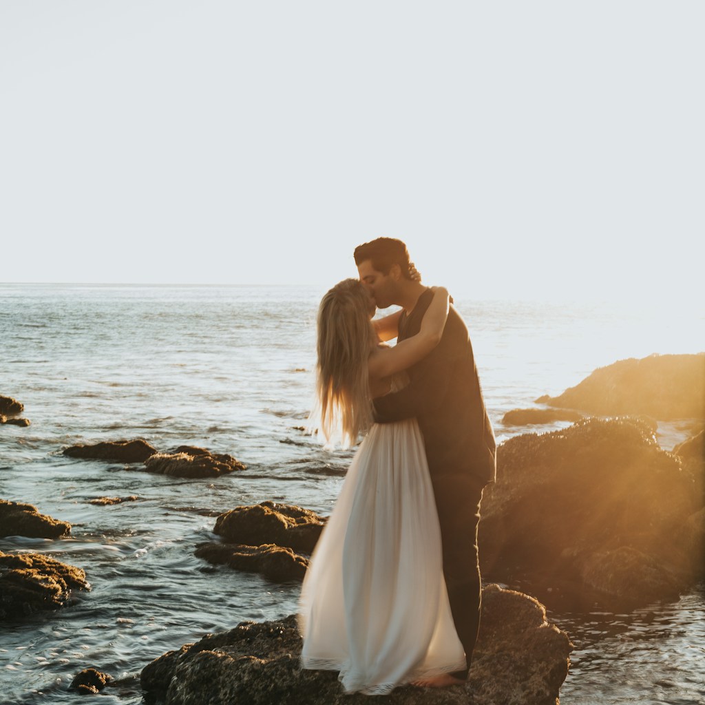 man and woman kissing on top of gray rock at beach