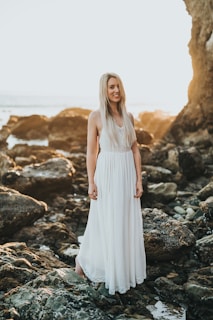 selective focus photography of woman standing at sea rock formation