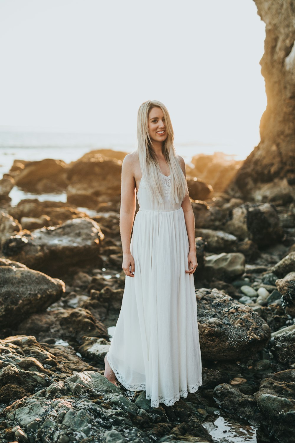 selective focus photography of woman standing at sea rock formation