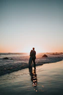 silhouette photo of couple standing on beach watching sunset