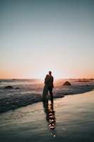 silhouette photo of couple standing on beach watching sunset