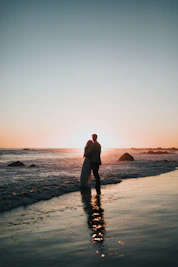silhouette photo of couple standing on beach watching sunset