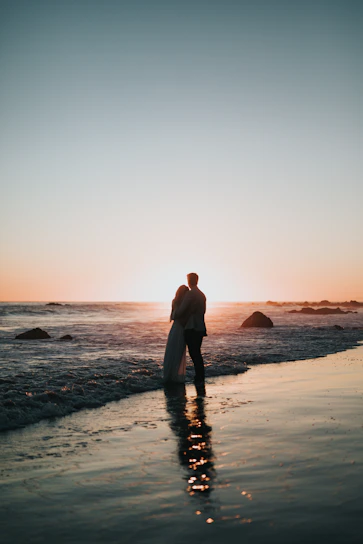 A warm, candid photo of a couple enjoying a sunset on a beach, capturing genuine smiles and soft natural light.