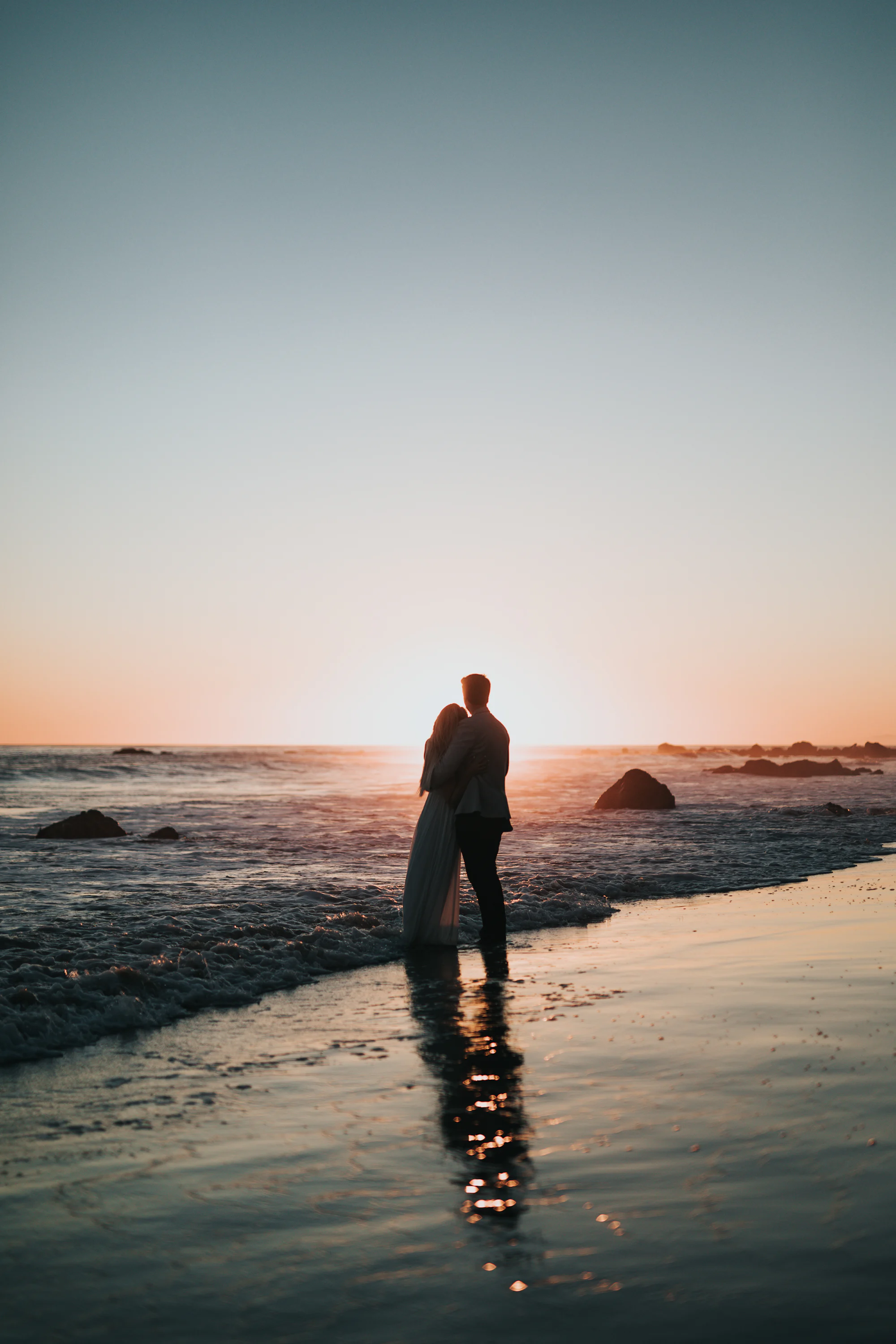 Pareja en silueta frente al mar al atardecer, en una boda íntima en la playa