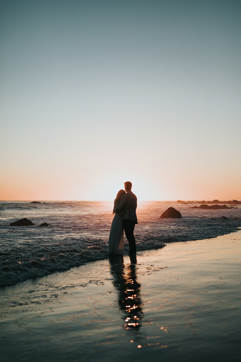 silhouette photo of couple standing on beach watching sunset