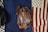 A brown leather jacket is laid out flat on a dark blue fabric with part of a folded American flag visible on the right. On the left, there is a glimpse of another dark-colored item, possibly another jacket or blanket.