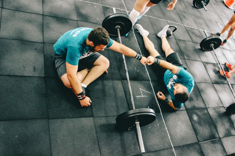 Two training partners fist-bumping on the gym floor between barbells
